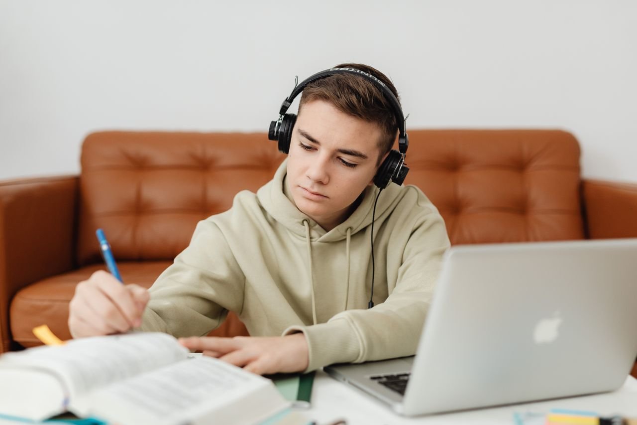 Teenage boy with headphones, focused on studying, using a laptop indoors.